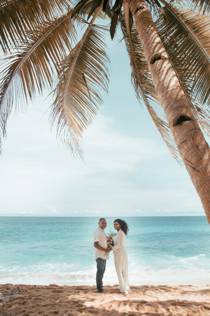 A married couple stand in front of the ocean at a tropical destination.