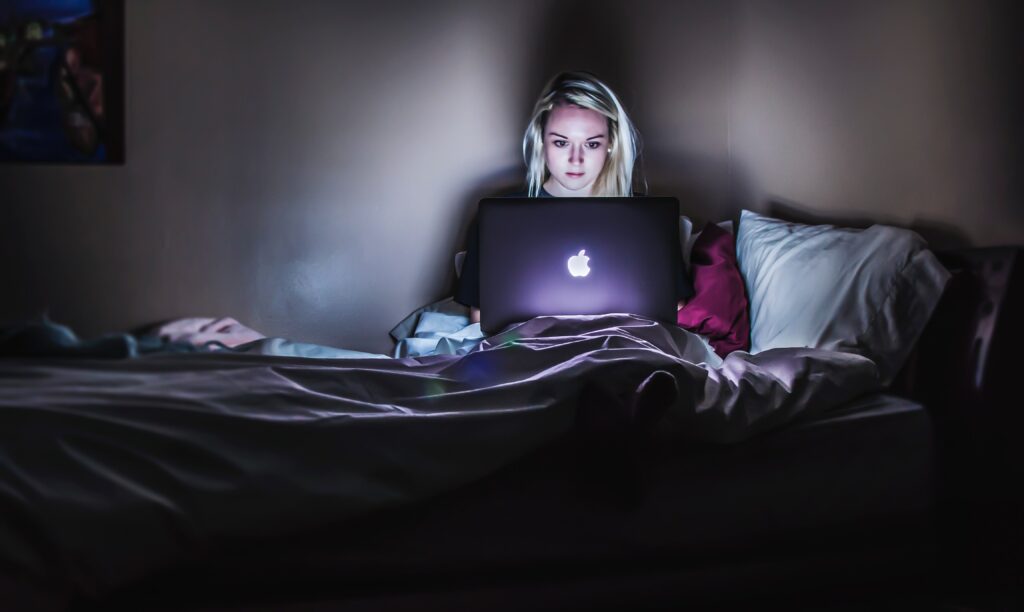 A woman working on a laptop at night in bed. Represents wedding burnout.